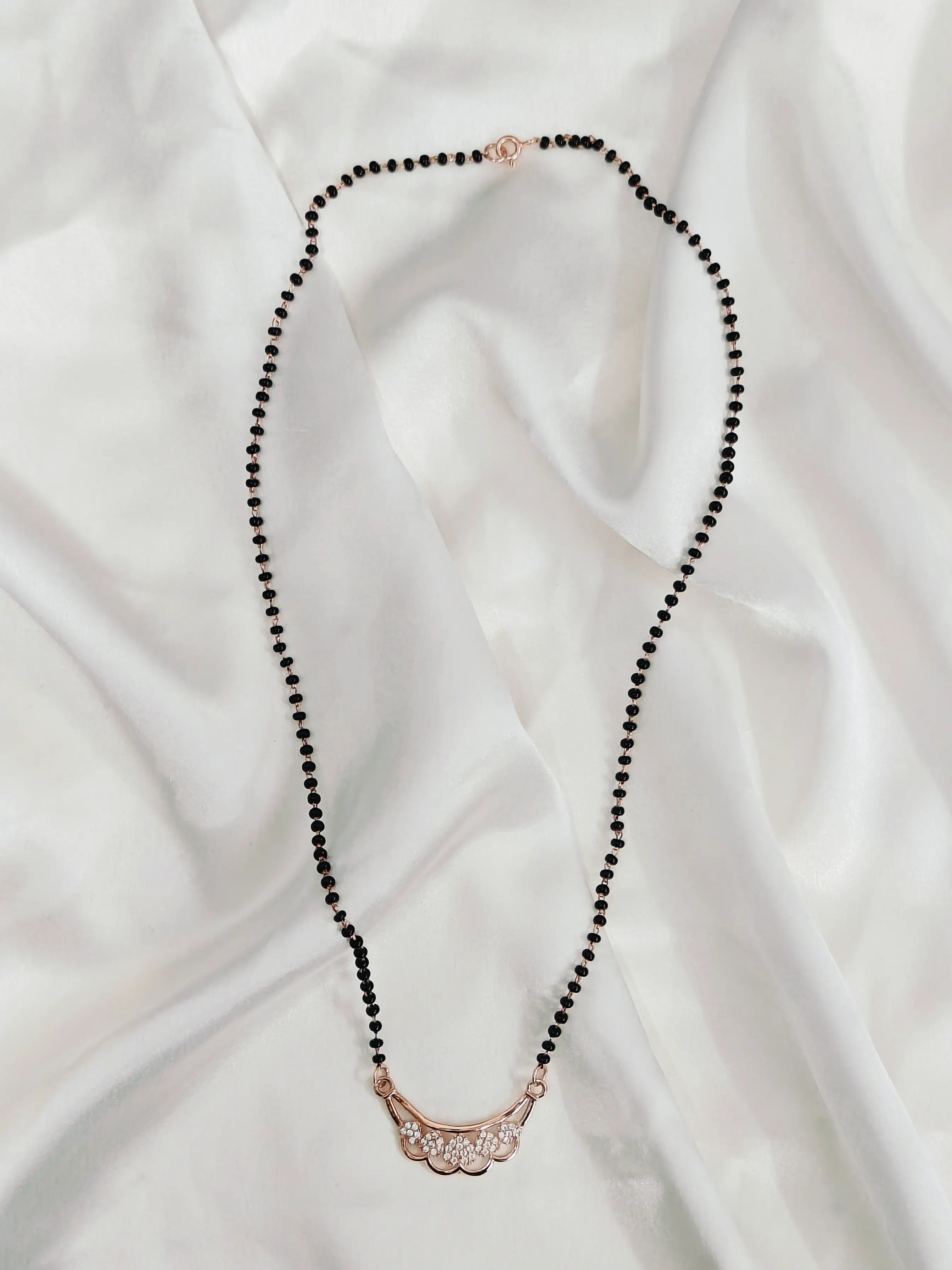 Black beaded necklace with a rose gold clasp on a white fabric background